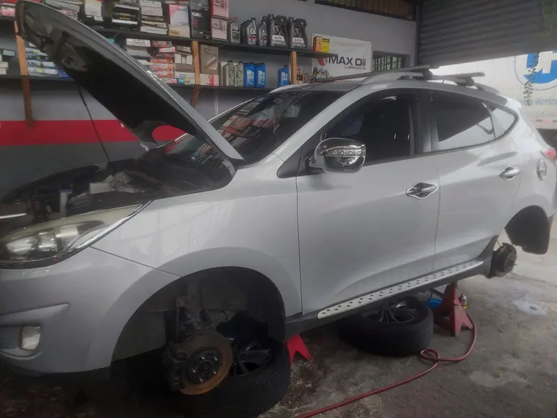 SUV plateado sin ruedas delanteras y con los frenos a la vista, frente al estante de aceites