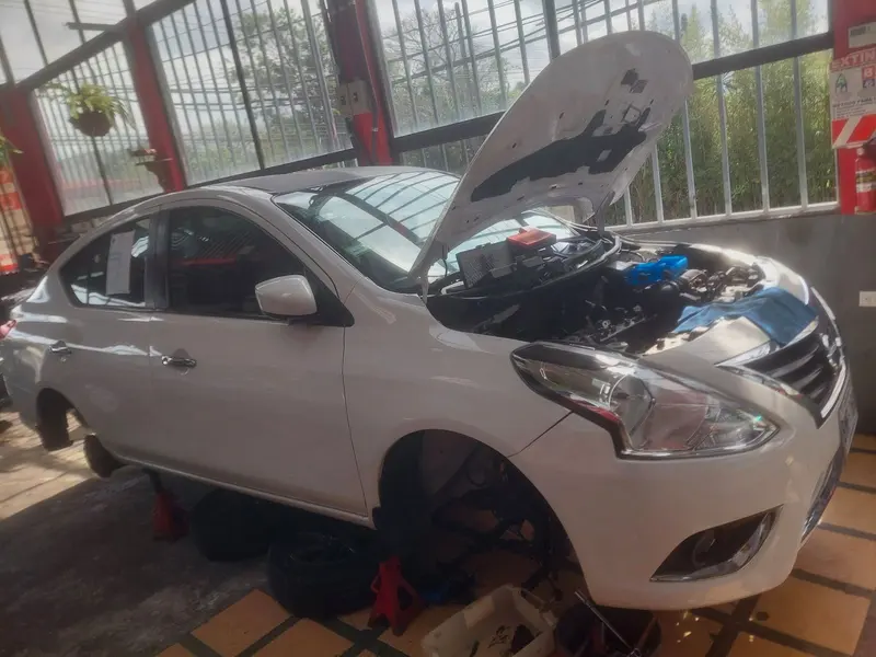 Sedán blanco con el capó abierto sobre burras, dentro del taller